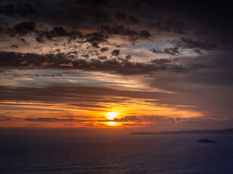 Aerial view of Sharp Point Lookout at sunset, with dramatic clouds over the ocean, golden light reflecting on the water, and the rugged coastline of Torndirrup, Western Australia, Australia.