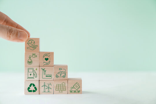 Hands holding wooden blocks with green sustainable environmental icons, renewable energy concept

