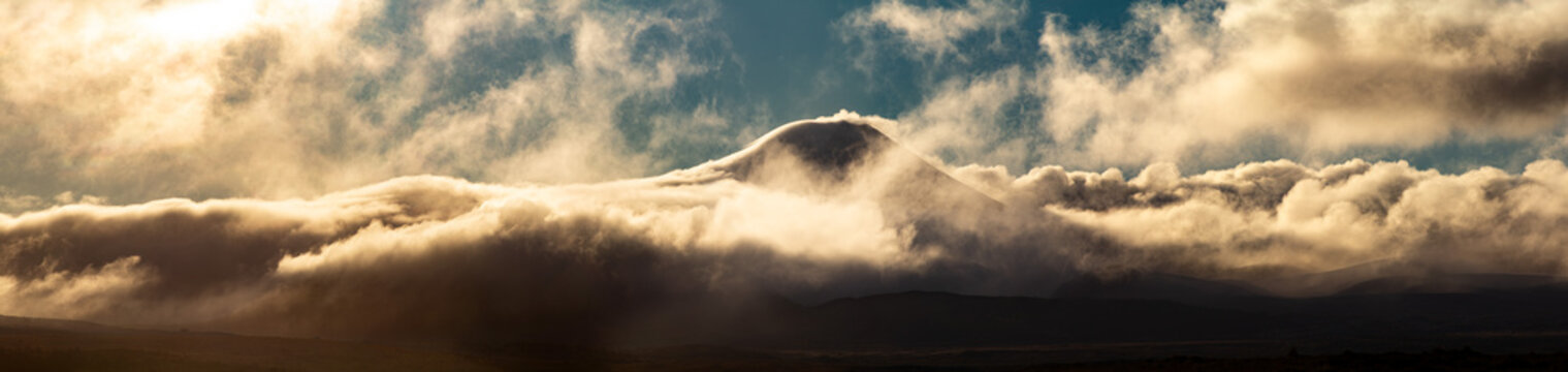 Mt Ngauruhoe volcano poking through cloud, panoramic view. Tongariro National Park, New Zealand. Active volcanic cone. Dramatic golden light.