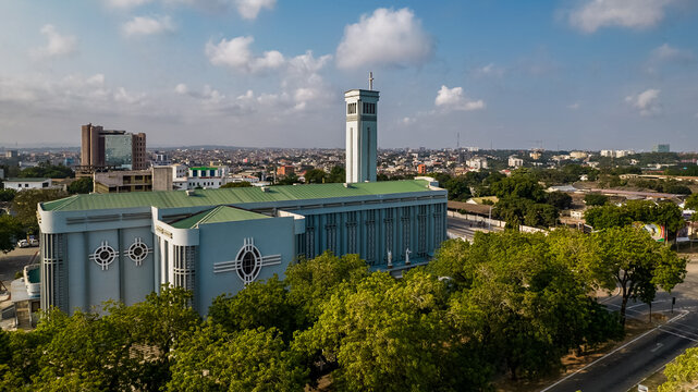 Aerial view of the Holy Spirit Cathedral with its distinctive blue facade and tall bell tower, surrounded by lush green trees and the urban cityscape of Accra, Greater Accra Region, Ghana.