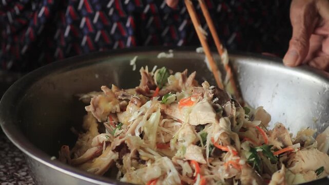 Close up video of a person using bamboo chopsticks to mix traditional shredded chicken salad with vegetables