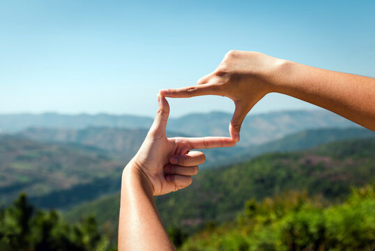 hand with a frame. hand framing view distant over sunset on mountain. Two hands cupped together, framing the vibrant golden sun setting over a distant mountain range, with dramatic clouds filling.
