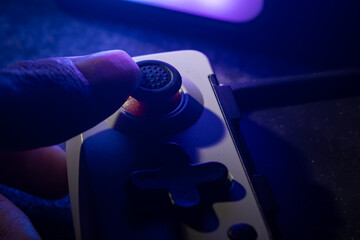 Close up of a gamer thumb controlling the analog joystick of a mobile gamepad under neon blue and purple lights © Nguyen Tuan