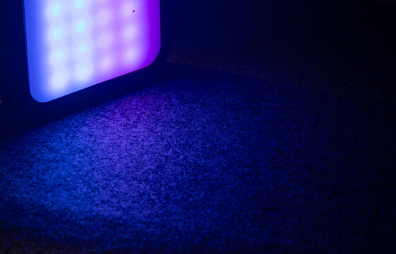 An RGB LED light panel casting a colorful purple and blue glow onto a dark textured ground surface