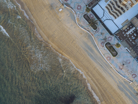 Aerial view of the sandy beach and patterned promenade with palm trees and buildings in Calp, Valencian Community, Spain.