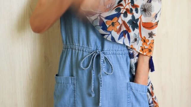 An elderly lady in a denim dress throws a light colorful scarf over her shoulder
