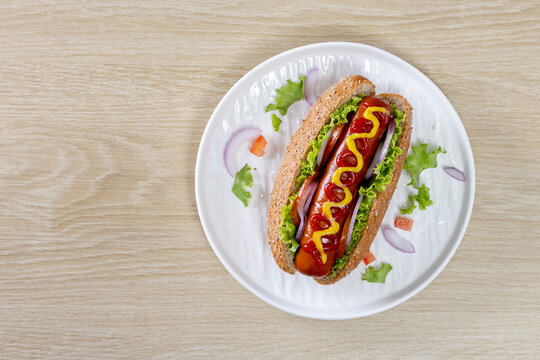 Hot dogs topped with mustard and ketchup on a white plate against a wooden table background.