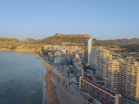 Aerial view of high-rise apartment buildings along the sandy beach and the Mediterranean Sea with mountains in the background in Calp, Valencian Community, Spain.