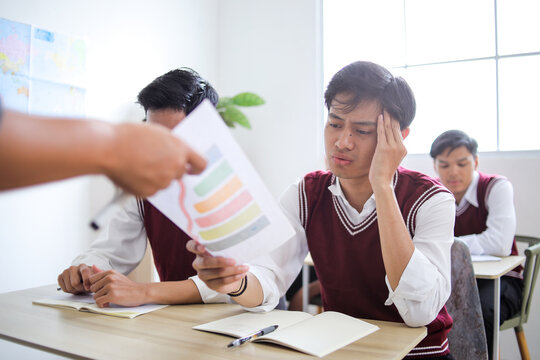 Stressed Male Student Holds Bad Test Report with Colorful Chard While Teacher Passes Back Papers