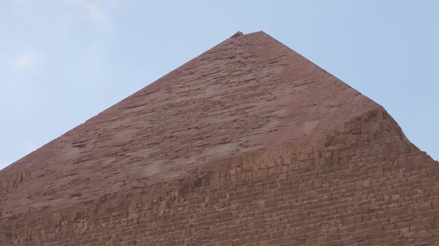 close up shot of the Pyramid of Khafre at the Giza Necropolis, showcasing the weathered stone blocks and the distinct capstone, set against a clear blue sky.