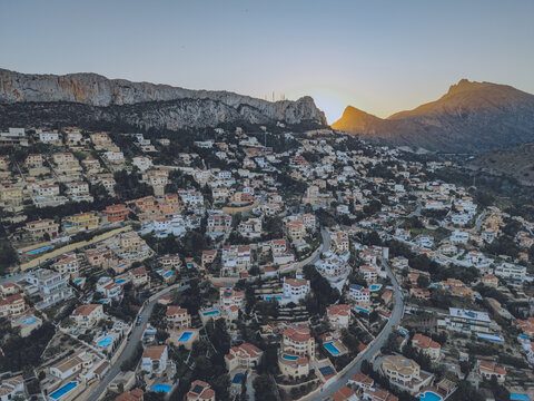 Aerial view of residential houses with swimming pools nestled on a hillside at sunset with the rocky Penyal d'Ifac mountain in the background in Calp, Valencian Community, Spain.