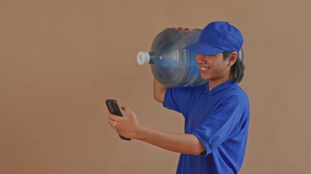 Smiling water delivery man using his smartphone while carrying large gallon jug on his shoulder