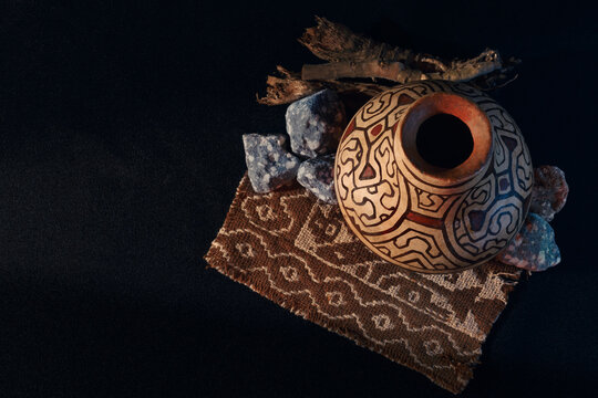 Handcrafted ceramic pot with intricate, swirling patterns. Dark background highlights the pot's earthy tones and textures. Ancient stones and weathered wood frame the pot's rustic charm