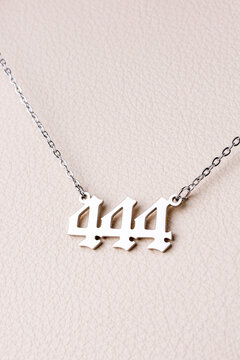 Close-up of a silver pendant with the number 444 on a chain, set against a luxurious white leather background.