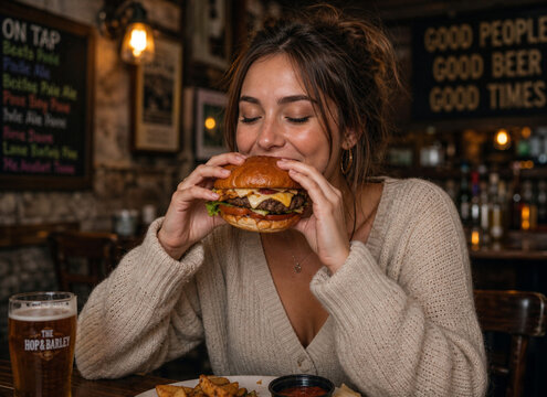 Young woman enjoying cheeseburger and beer at pub