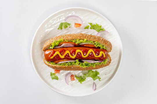 Hot dogs topped with mustard and ketchup on a white plate against a white background.