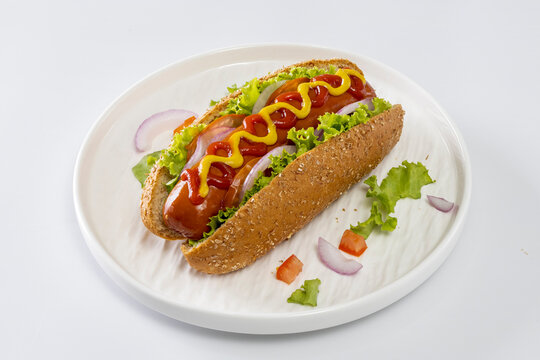 Hot dogs topped with mustard and ketchup on a white plate against a white background.