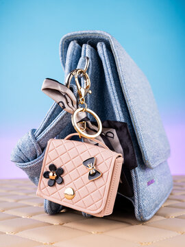 Close-up of a leather mini bag-shaped keychain with bow and charms on a  blue bag. Elegant and charming accessory.