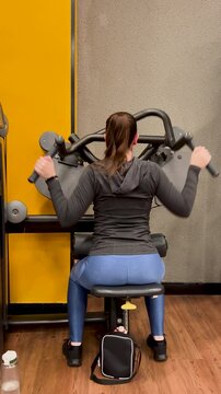 Rear view of woman pulling overhead handles on lat pulldown machine in commercial gym, fitness, gym equipment, muscle building and workout.