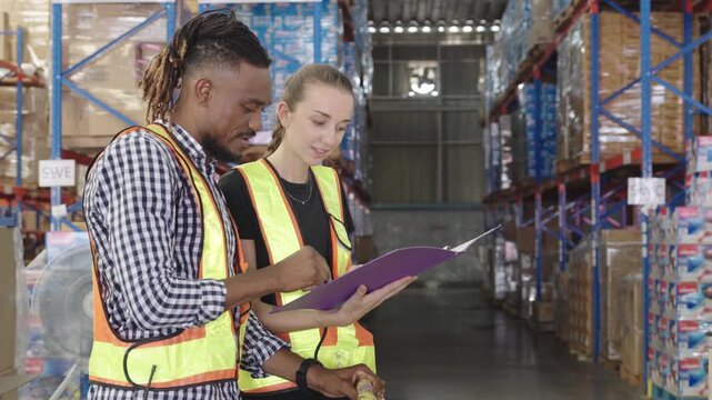 Man and woman collaborate reviewing documents within brightly lit warehouse environment while wearing high-visibility vests-showcasing operational efficiency and safety protocols during industrial ins