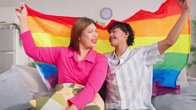 Portrait of transgender woman and partner holding rainbow flag in house.