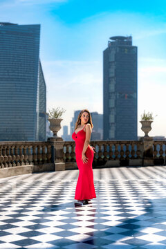 Young smiling latina woman posing confidently and stylishly while enjoying the view toward Reforma avenue at Castillo de Chapultepec in Mexico City, wearing a fitted vibrant red dress and sunglasses