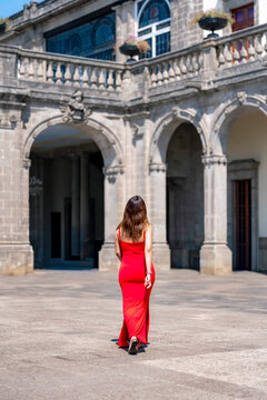 Unrecognized young latina woman walking confidently and calmly toward the museum entrance at Castillo de Chapultepec in Mexico City, wearing a vibrant fitted red dress with elegant style