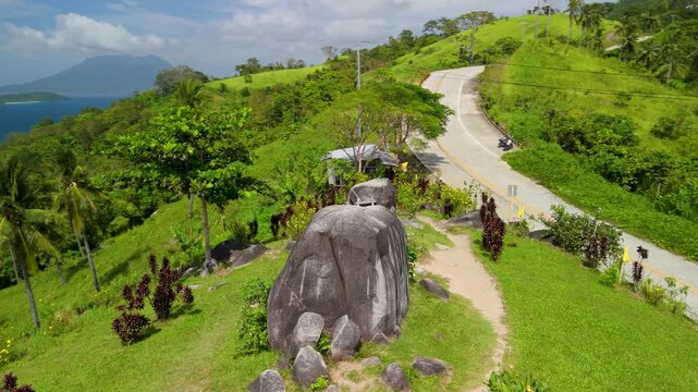 Aerial parallax around Bato ni Ningning landmark boulders in San Vicente Palawan with lush green hills, winding road and blue ocean panorama