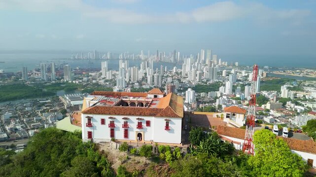 Aerial orbital shot of white colonial Convento de la Popa hilltop convent against sprawling Cartagena city skyline with bay and mangroves behind in Colombia