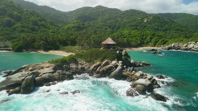 Aerial parallax over iconic Cabo San Juan thatched mirador on rocky headland between twin turquoise beaches at Parque Tayrona near Santa Marta Caribbean Colombia