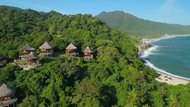 Aerial parallax over thatched eco bungalows on jungle headland above Caribbean beach and surf at Playa Ca&ntilde;averal in Parque Tayrona near Santa Marta Colombia