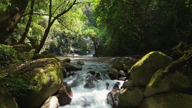 Aerial flyover close above whitewater rapids of clear mountain river rushing over mossy granite boulders at Cascada Escondida in jungle of Minca near Santa Marta Colombia