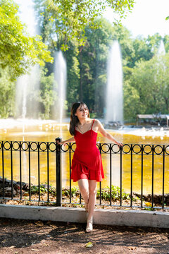 Young smiling latina woman posing relaxed, by the central fountain at Parque Mexico in Condesa, Ciudad de Mexico enjoying a sunny day surrounded by water, greenery wearing a bright red dress