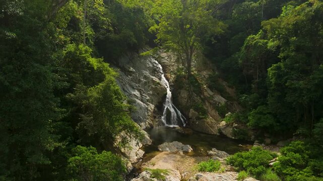 Slow aerial approach to tall Quebrada Valencia waterfall cascading down rocky cliff into pool surrounded by lush green jungle near Santa Marta Colombia