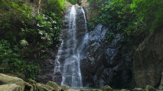 Push in with tilt up reveals tall tropical waterfall cascading down rocky cliff through lush jungle at Teyumakke in Parque Tayrona near Santa Marta in Sierra Nevada Colombia