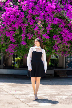 Young smiling latina woman posing relaxed, cheerful outdoors at Parque Mexico in Condesa, Ciudad de Mexico surrounded by vibrant bougainvillea flowers, wearing a black dress, white blouse, sunlight