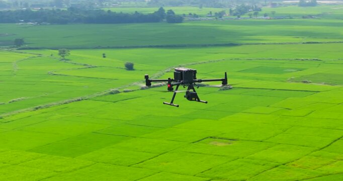 An aerial orbit shot circling a mapping and engineering drone as it hovers in the sky, showcasing a wide view of the vast plain lands and rural Terai landscape below.