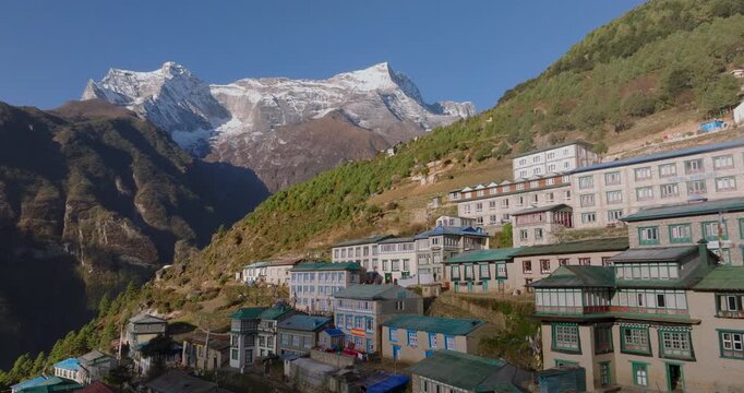 Namche Bazaar, Everest region, Nepal. An aerial lateral tracking shot sweeping across the famous Sherpa town, showcasing traditional colorful lodges, with towering snow-capped Himalayan mountains
