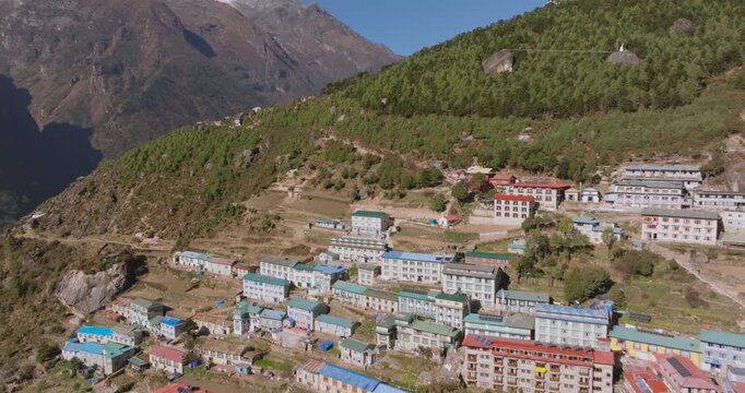 Namche Bazaar, Nepal, aerial shot starting over colorful village houses and massive green hills, moving toward the dramatic snow-capped summit of Kongde Ri peak, sunny day and prominent landscape