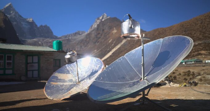 A static close-up shot of parabolic solar cookers boiling water in kettles at a high-altitude mountain lodge facility in Namche Bazaar, Everest, Nepal.