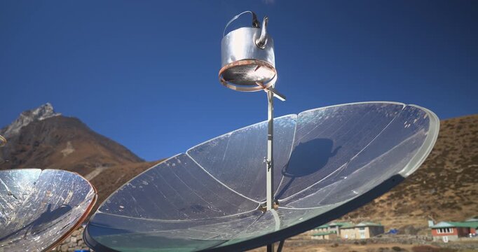 A low-angle static shot focusing on a single metal kettle boiling water on a parabolic solar cooker outside a high-altitude mountain lodge in Namche Bazaar, Everest, Nepal.