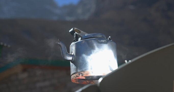 Everest, Nepal, static close-up shot of steam vaporizing from the spout of a hot metal kettle boiling under the intense heat of a parabolic solar cooker in a high mountain altitude