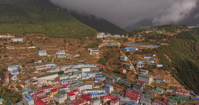 Hyperlapse of Namche, Bazar, Nepal, revealing fast-moving clouds above green hills and the tiered houses with colorful rooftops of the Himalayan village.