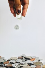 A fast-moving coin slipping from a person's fingertips into a scattered arrangement of diverse Malaysian coins, illustrating continuous saving habits, cash drainage, or digital-to-cash transitions. © Akram