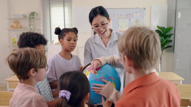 Asian female teacher using educational globe teaching students in classroom.
