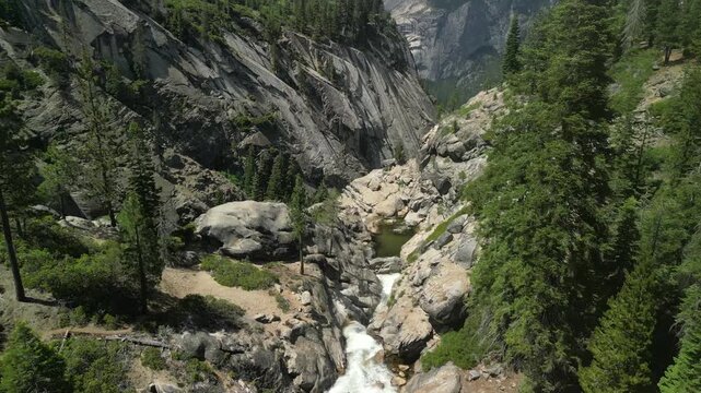 Aerial shot of Yosemite Valley featuring cascading waterfall surrounded by granite cliffs, dense forest, and dramatic mountain landscape in California&rsquo;s Sierra Nevada.