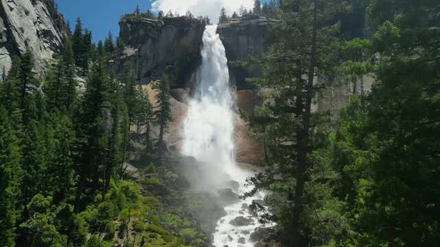 Aerial shot of Yosemite Valley featuring cascading waterfall surrounded by granite cliffs, dense forest, and dramatic mountain landscape in California&rsquo;s Sierra Nevada.