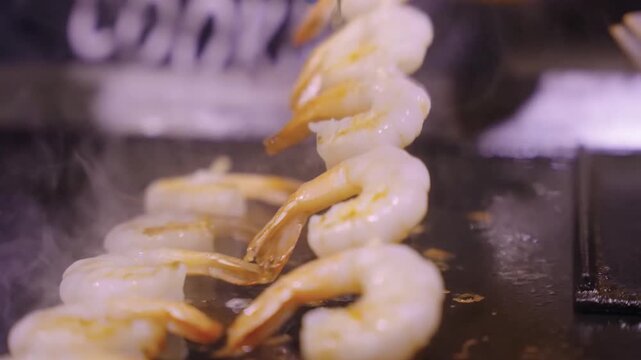 High-quality footage capturing the lively sizzle of peeled and de-veined shrimp cooking on a hot professional grill. The steam and gentle browning highlight the culinary process of preparing fresh sea