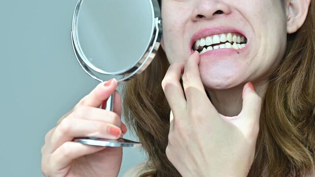 Asian woman using a mirror for checking her mouth and teeth.