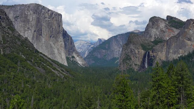 Static shot of Yosemite Valley with a waterfall flowing through granite cliffs and forested landscape in California.
